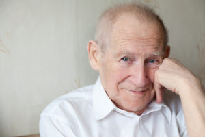 face portrait of a cheerful smiling senior man with his arm near his face